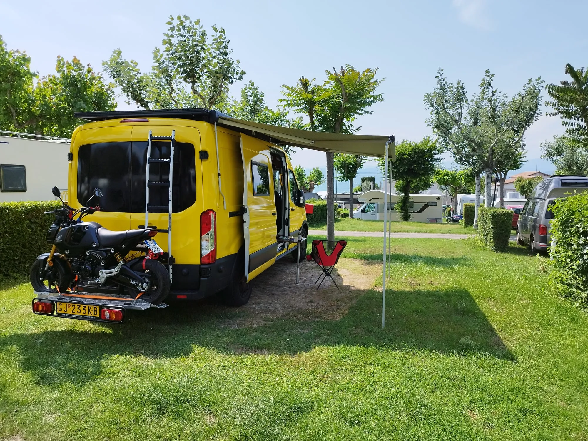 Auf dem Campingplatz: Van mit Markise und Motorrad am Heck